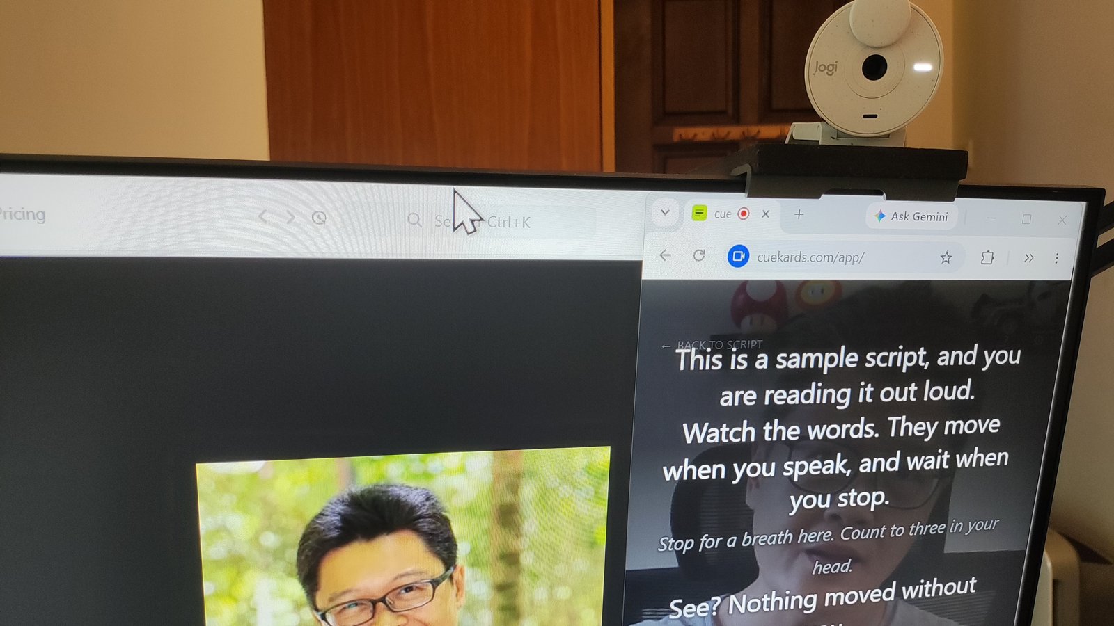 A monitor with a webcam clipped to the top right. Directly under the webcam, cuekards fills a narrow browser window with large white script text near the top, and the Zoom app sits in the window to its left